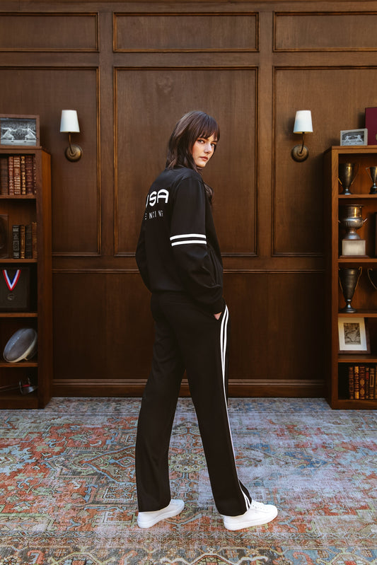 Person wearing a black tracksuit with 'VSA' branding in a room with wooden paneling and bookshelves.