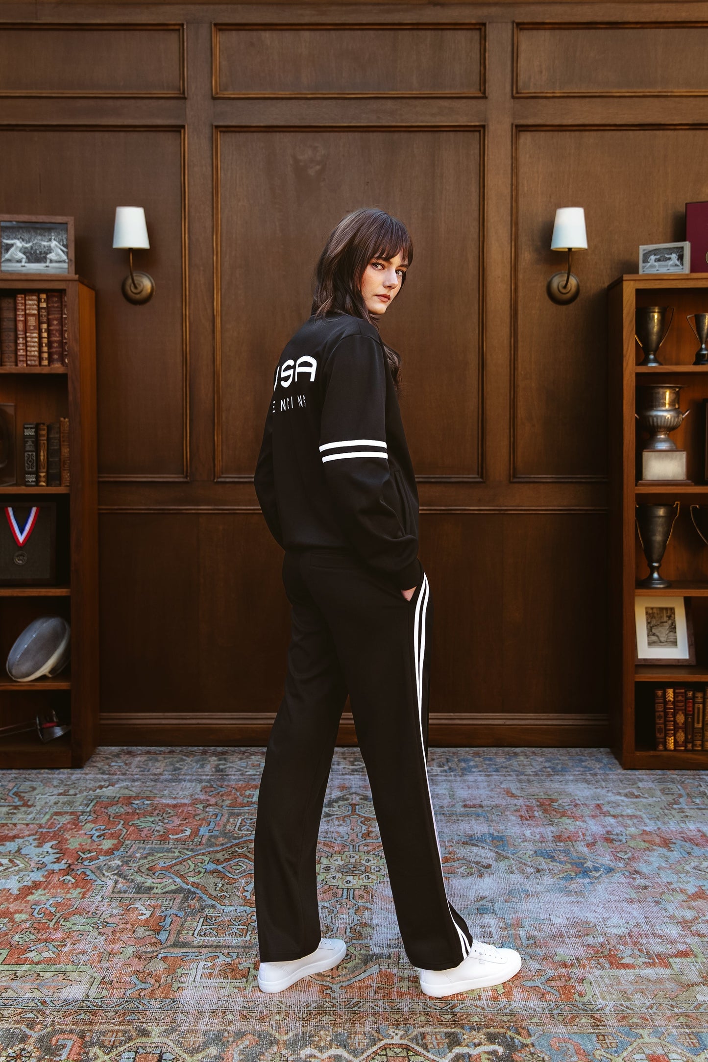 Person wearing a black tracksuit with 'USA' branding in a room with wooden paneling and bookshelves.