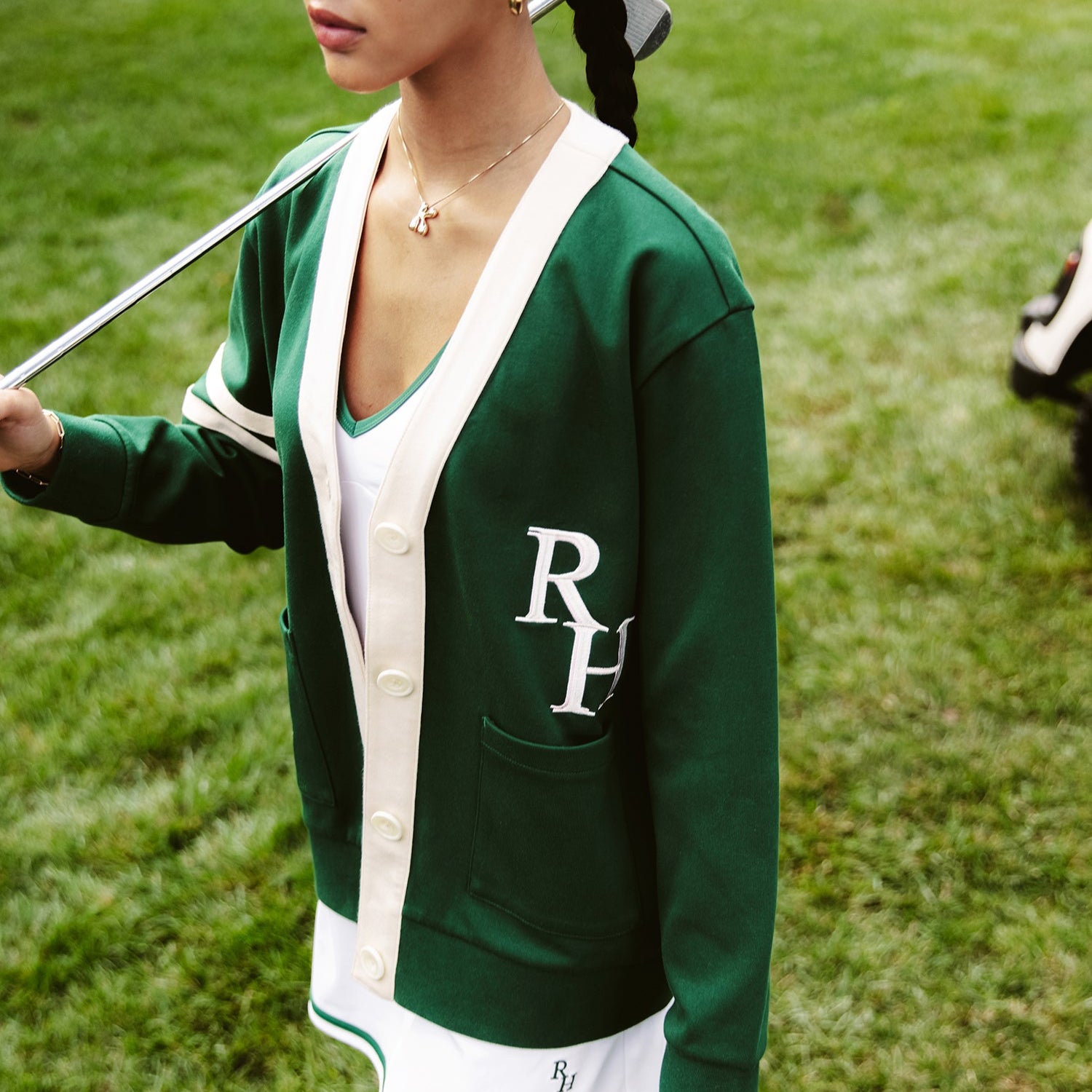 A woman in a green cardigan at a country club, wearing a golf outfit. 